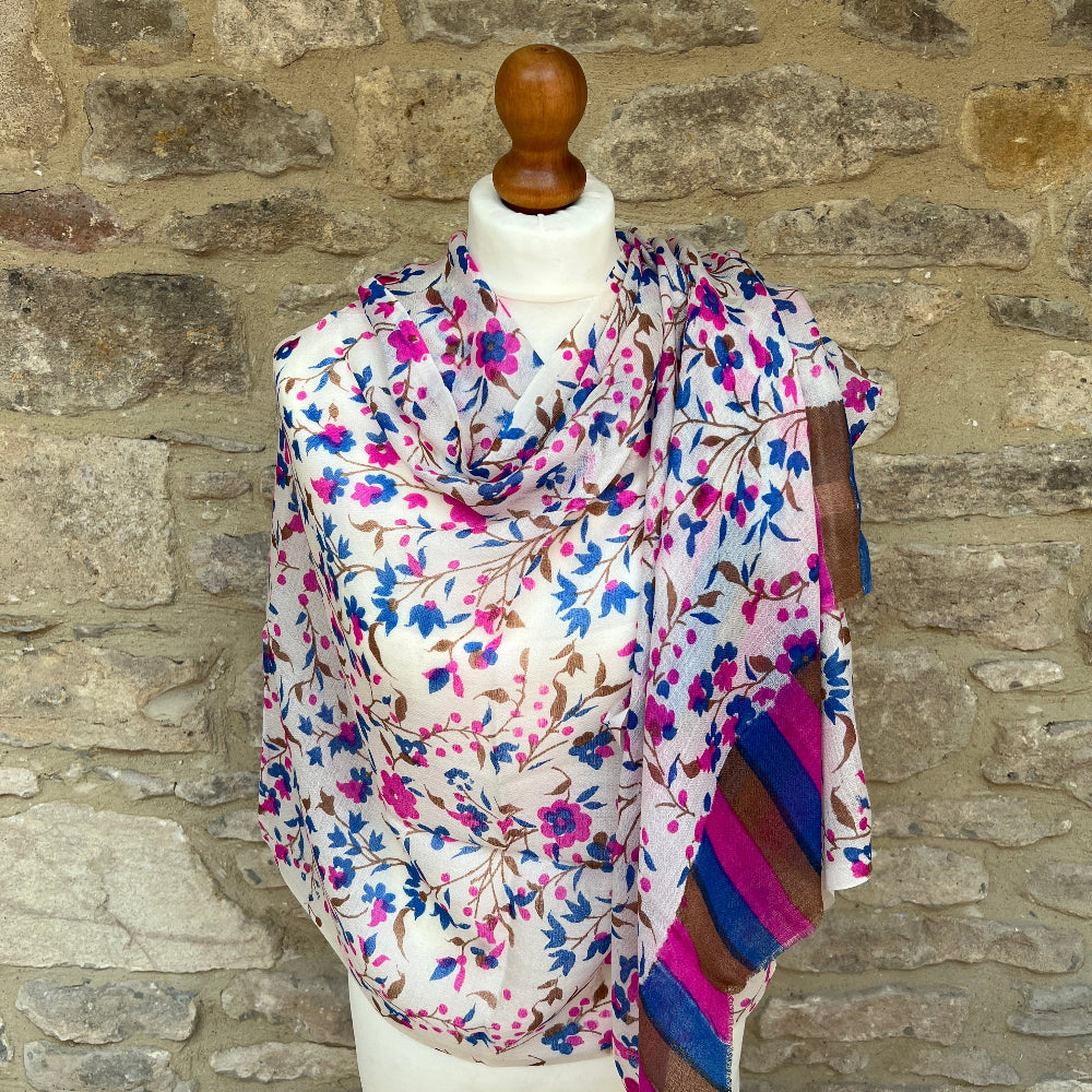 A multicoloured gossamer light floral patterned cashmere pashmina scarf on a mannequin against a stone wall background