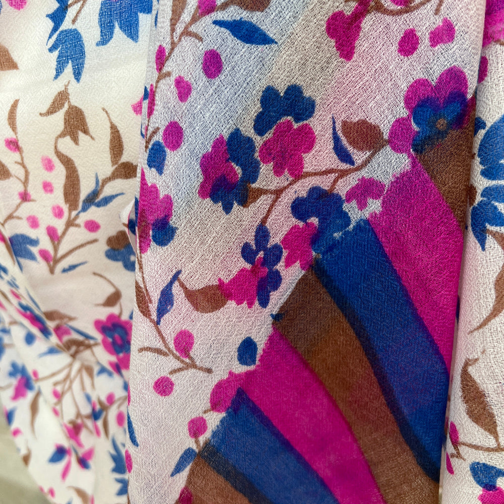 A multicoloured gossamer light floral patterned cashmere pashmina scarf on a mannequin against a stone wall background