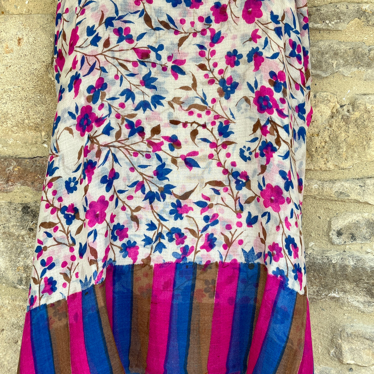 A multicoloured gossamer light floral patterned cashmere pashmina scarf on a mannequin against a stone wall background