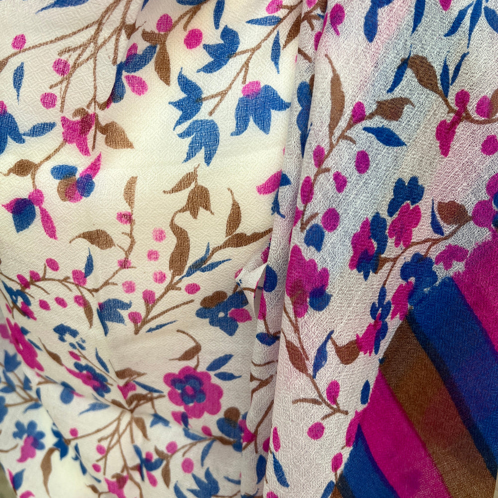 A multicoloured gossamer light floral patterned cashmere pashmina scarf on a mannequin against a stone wall background