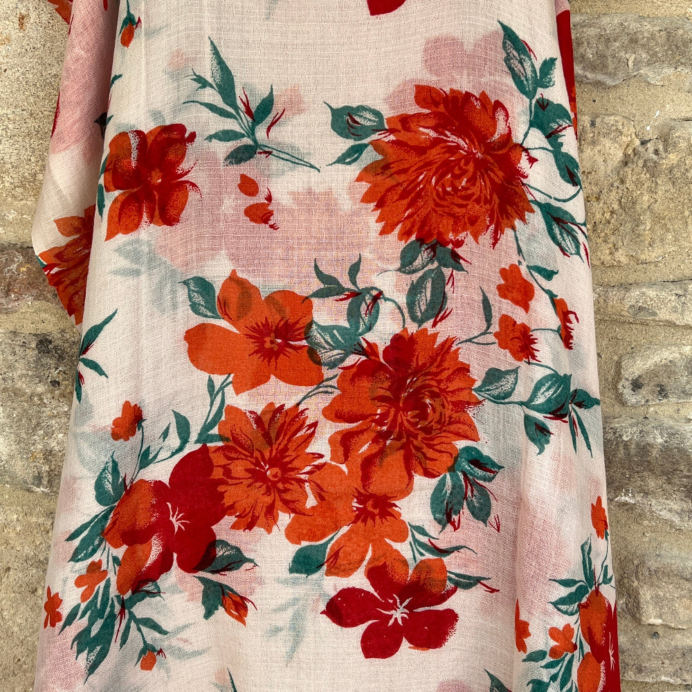 An orange floral cashmere pashmina scarf against a stone wall background.