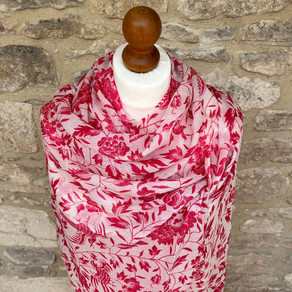 Red floral patterned cashmere scarf on a mannequin against a stone wall background