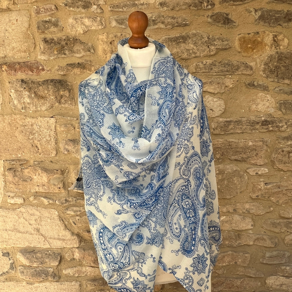Mannequin wearing a blue and white paisley patterned cashmere pashmina scarf against a stone wall.