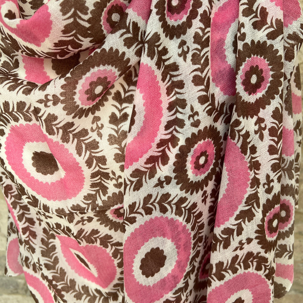 Cashmere pashmina with pink and brown circular pattern on a mannequin against a stone wall backdrop. 