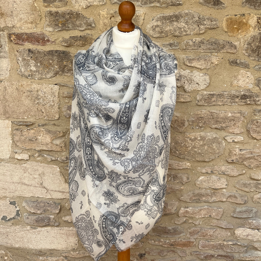 Paisley patterned cashmere scarf on a wooden mannequin against a stone wall background