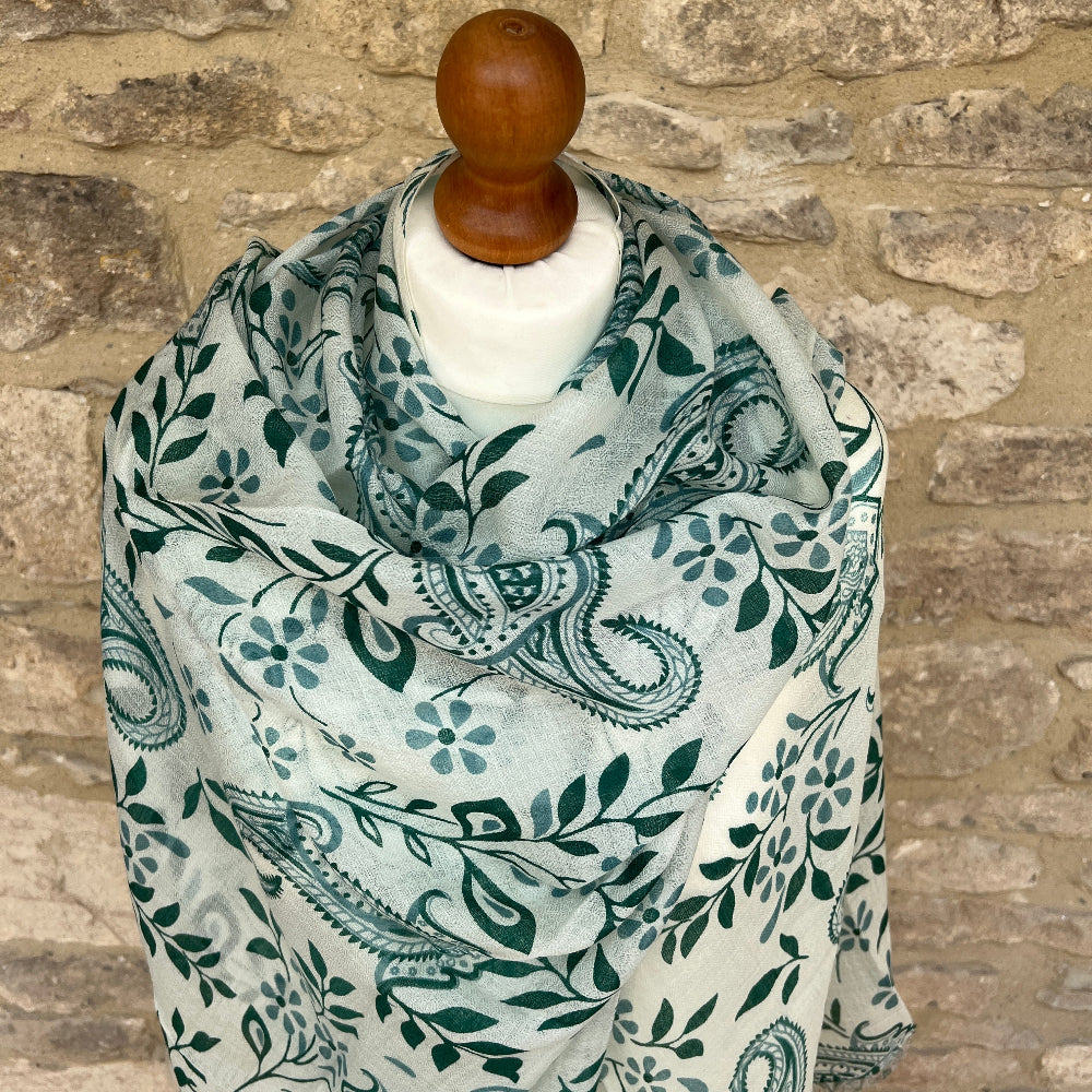 Cashnere pashmina scarf with green paisley leaf pattern draped over a mannequin against a stone wall.