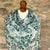 Cashnere pashmina scarf with green paisley leaf pattern draped over a mannequin against a stone wall.