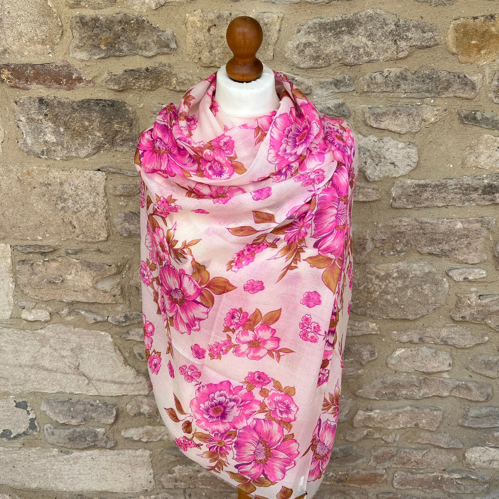 Cashmere pink floral pashmina scarf on a mannequin against a stone wall background.