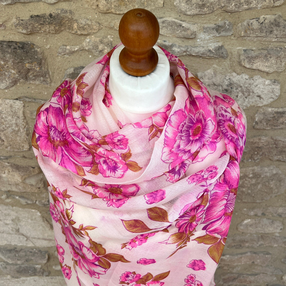 Cashmere pink floral pashmina scarf on a mannequin against a stone wall background.