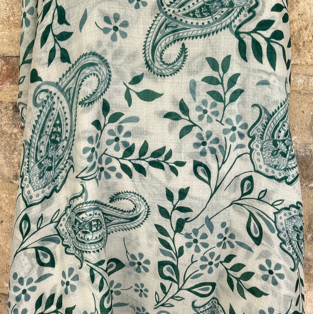A cashmere pashmina scarf with a leaf and paisley design against a stone wall background.