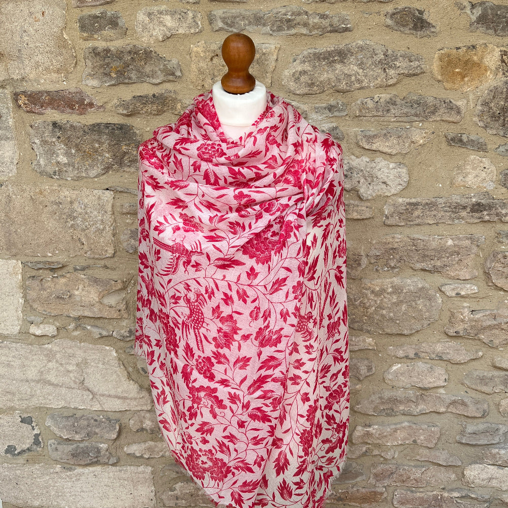 Pink floral patterned cashmere scarf on a mannequin against a stone wall background