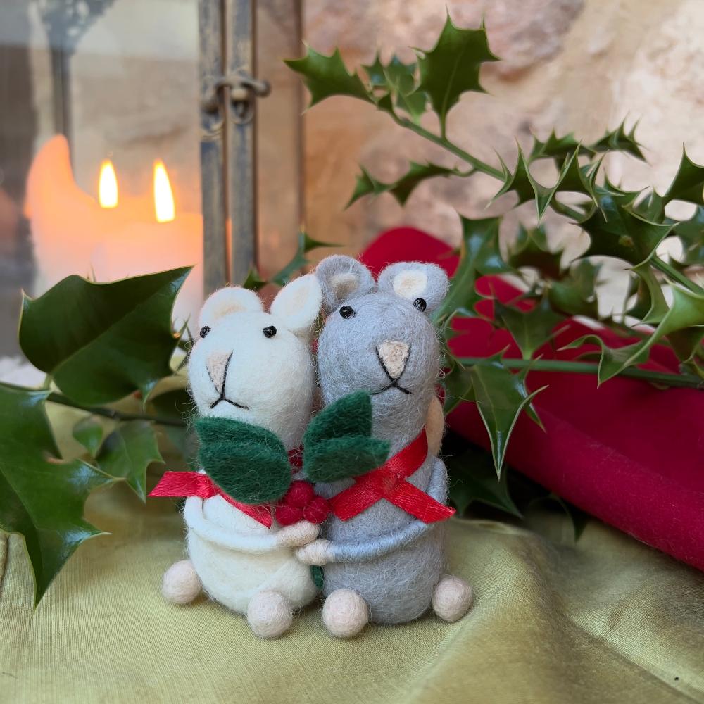 Introducing an enchanting duo of handcrafted felted wool mice, captured in a tender embrace this festive season.

Each mouse couple showcases hand embroidery and features poseable wired arms for display. Adorned with delicate red ribbon scarves and clutching sprigs of holly, these charming companions embody yuletide romance.

Their intertwined tails form a graceful heart—a poignant symbol of enduring affection. A refined addition to any Christmas collection, these artisanal pieces celebrate love.