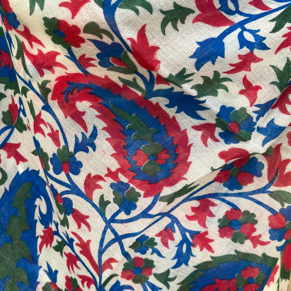 Close-up of a gossamer light, cashmere pashmina scarf with intricate floral pattern in red, blue, and green on a white background.