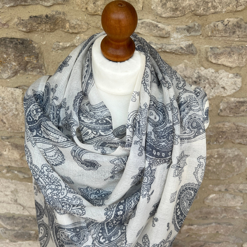 Paisley patterned cashmere scarf on a wooden mannequin against a stone wall background