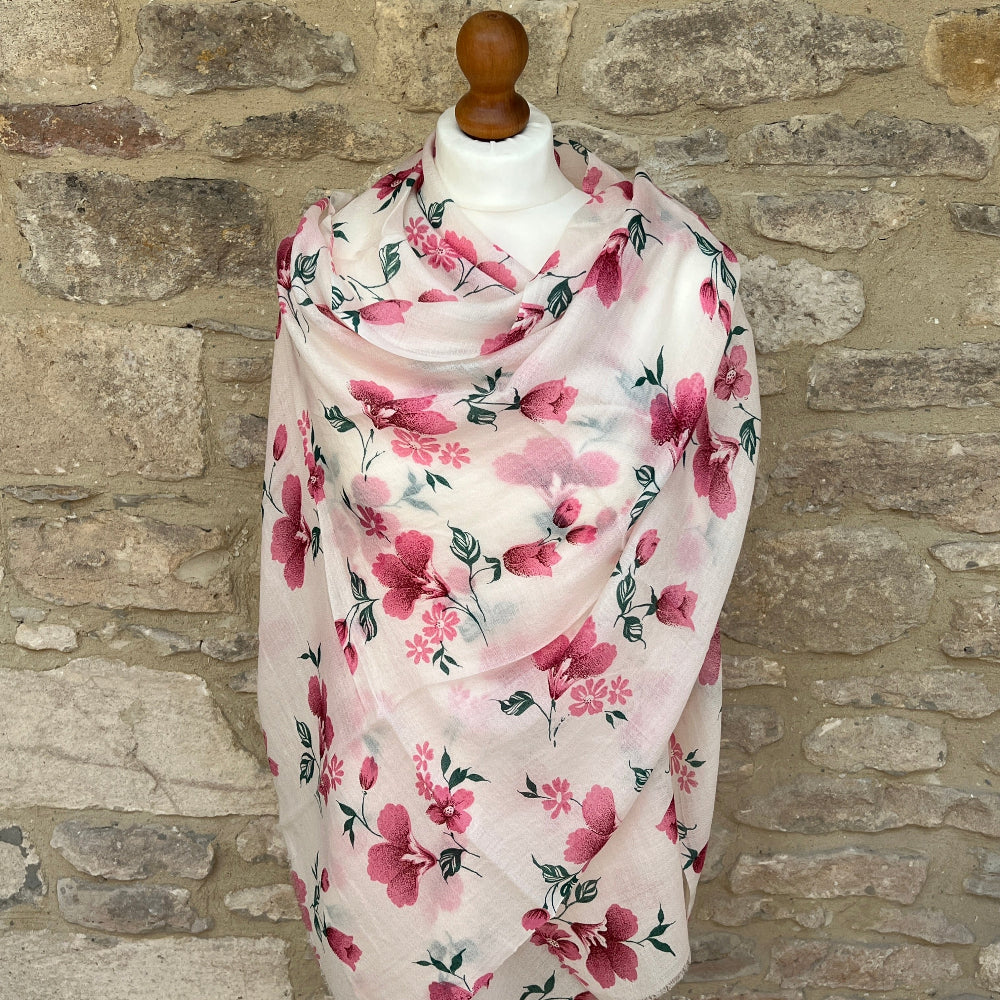 Delicate pink floral cashmere scarf on a mannequin against a stone wall background