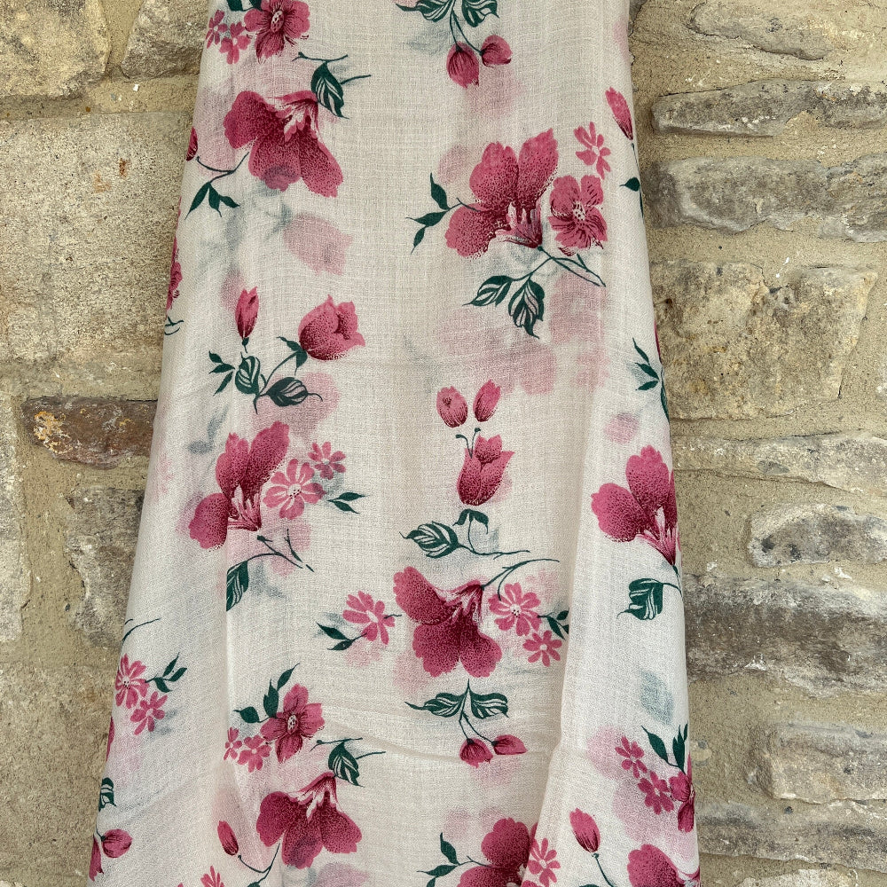 Delicate pink floral cashmere scarf on a mannequin against a stone wall background