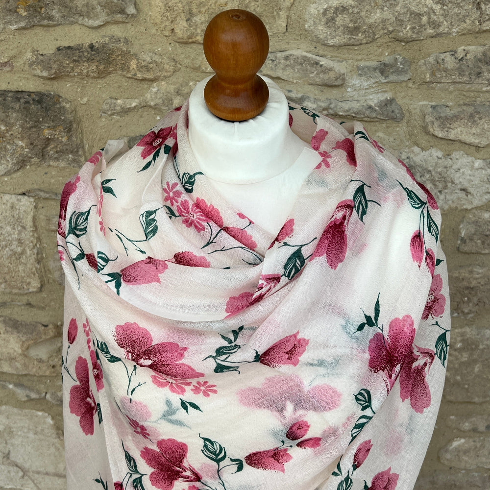 Delicate pink floral cashmere scarf on a mannequin against a stone wall background