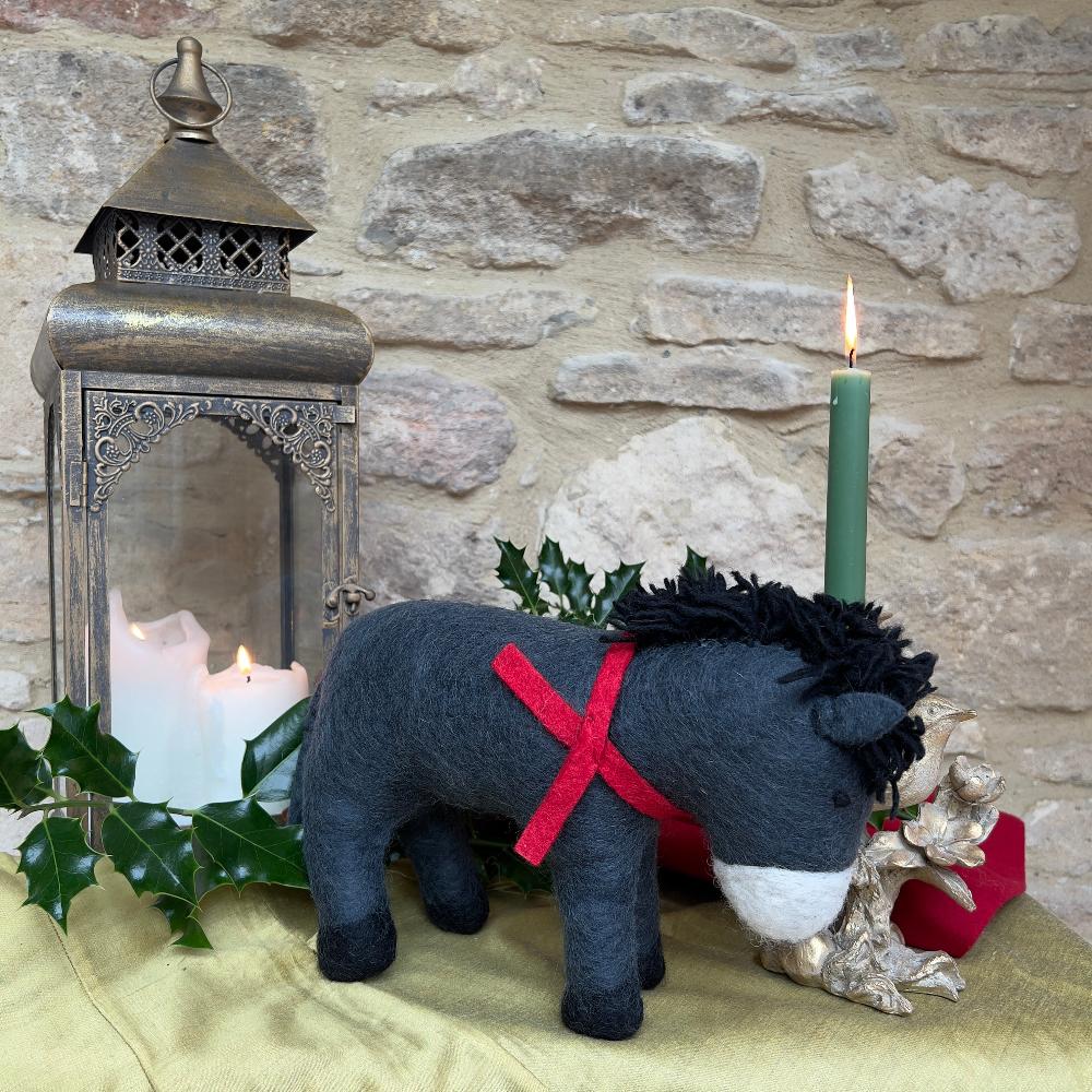 Discover the charm of our artisan, handcrafted felted wool larger sized Donkey.&amp;nbsp;

A delightful festive companion perfect for adding warmth to your seasonal décor. Each piece is handcrafted crafted from pure felted wool with hand-stitched details and dressed in a vibrant red scarf that captures the spirit of the season. Shown on gold silk fabric, against a cotswold stone wall with festive holly, candles and decorative accents. 