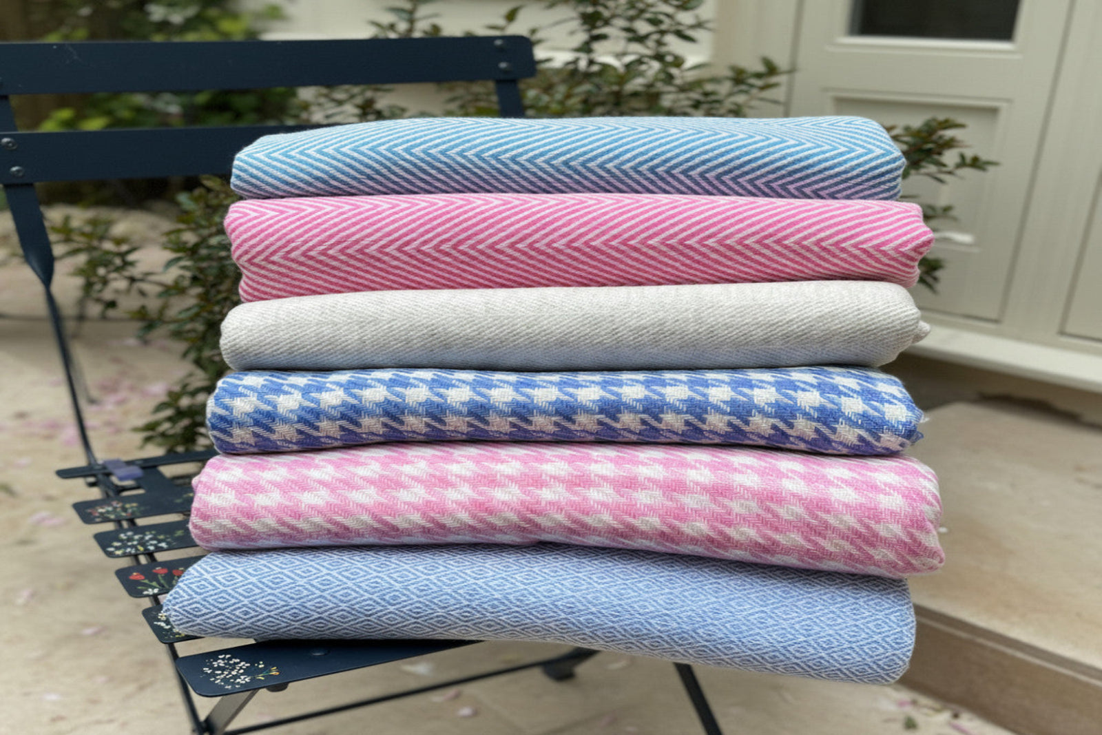 Folded cashmere throws & blankets in assorted patterns and colors on a chair outdoors.