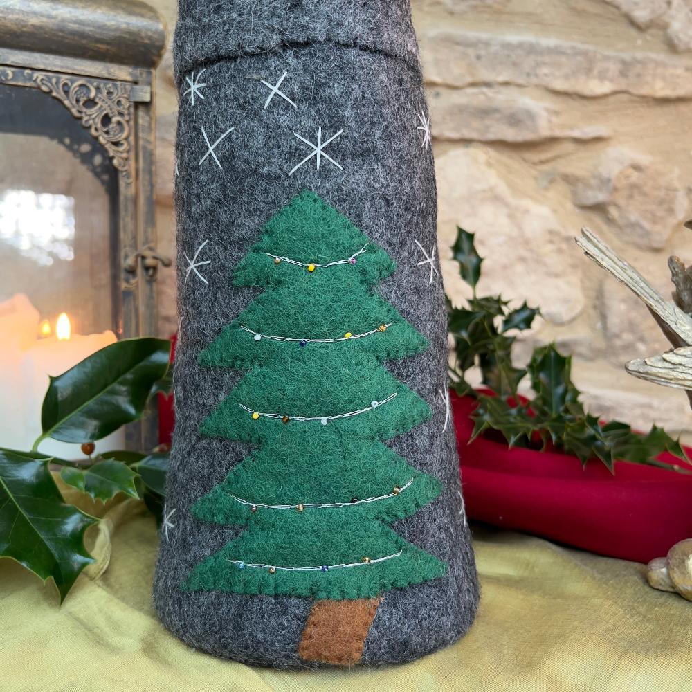 Bring festive charm to your home with this exquisite artisan handcrafted Father Christmas figure.

Meticulously created from premium felted wool, it showcases a luxuriously soft faux fur beard and intricate hand-stitched snowflake embellishments adorning the hat and body. The design features charming holly and berry appliqués on the hat, while the back displays an ornate Christmas tree decorated with sparkling beads. Shown with festive holly, candles and decorative items against a stone wall background. 