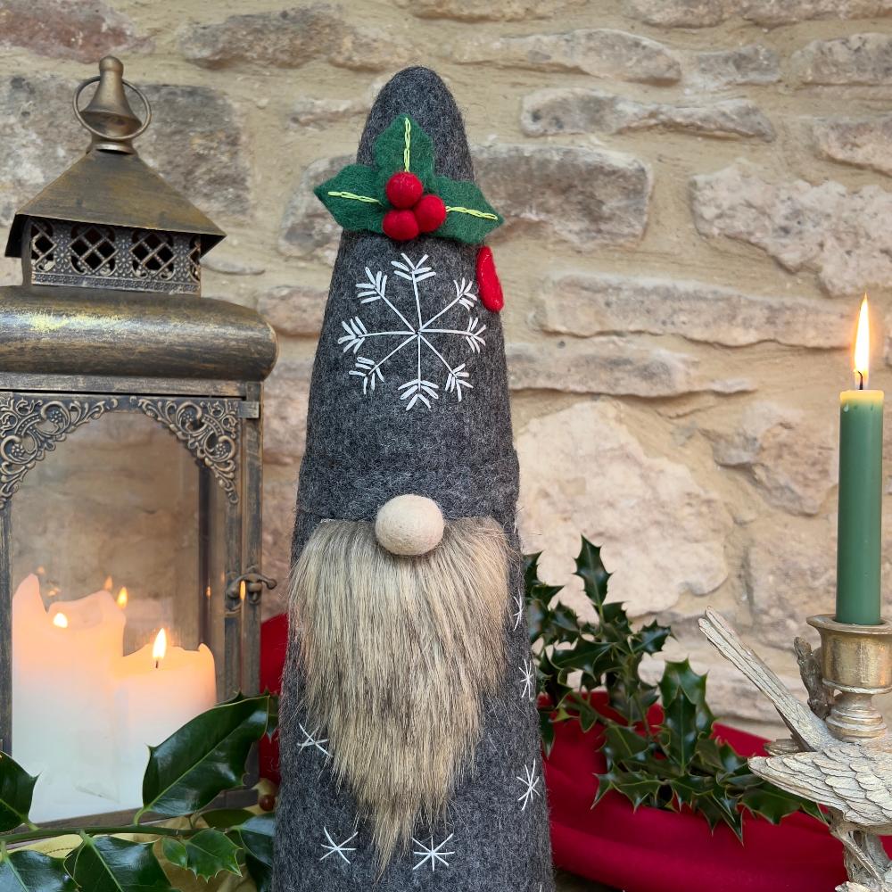 Bring festive charm to your home with this exquisite artisan handcrafted Father Christmas figure.

Meticulously created from premium felted wool, it showcases a luxuriously soft faux fur beard and intricate hand-stitched snowflake embellishments adorning the hat and body. The design features charming holly and berry appliqués on the hat, while the back displays an ornate Christmas tree decorated with sparkling beads. Shown with festive holly, candles and decorative items against a stone wall background. 