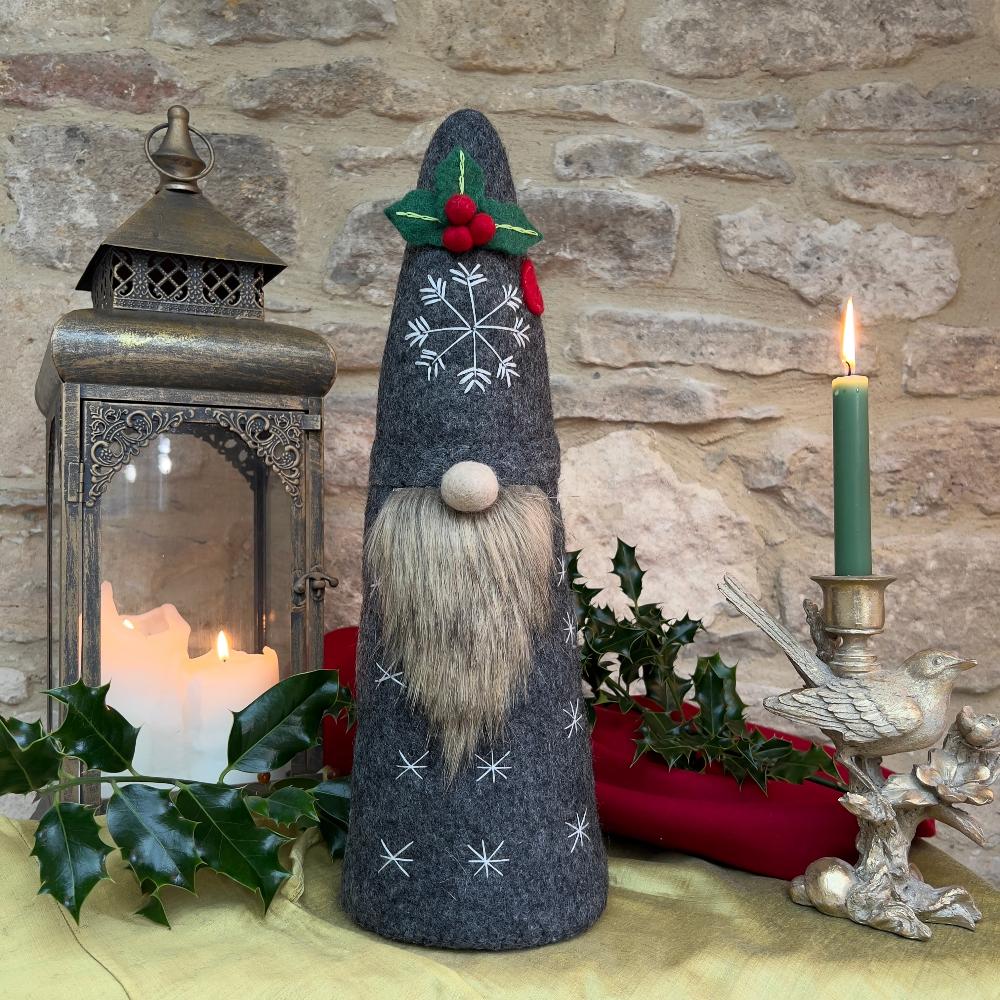 Bring festive charm to your home with this exquisite artisan handcrafted Father Christmas figure.

Meticulously created from premium felted wool, it showcases a luxuriously soft faux fur beard and intricate hand-stitched snowflake embellishments adorning the hat and body. The design features charming holly and berry appliqués on the hat, while the back displays an ornate Christmas tree decorated with sparkling beads. Shown with festive holly, candles and decorative items against a stone wall background. 
