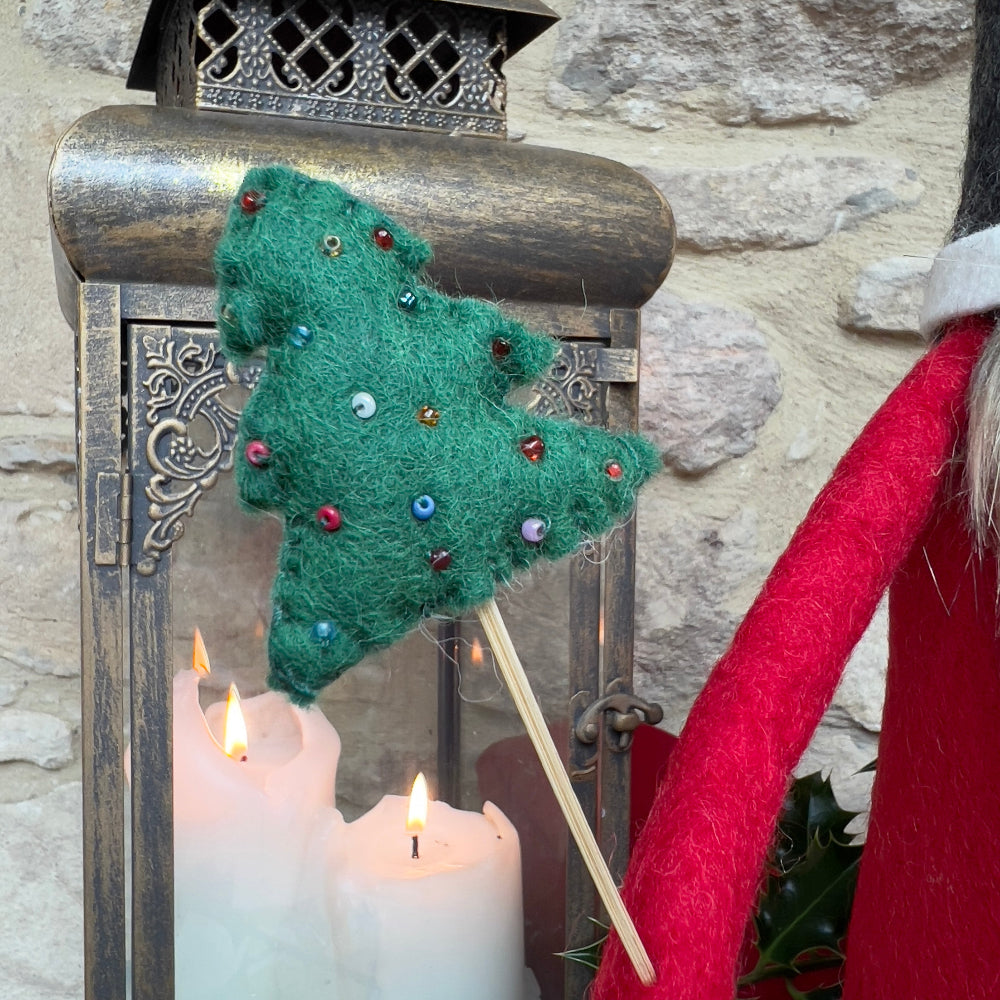 Elevate your festive décor with this exquisite handcrafted felted wool Father Christmas, a statement piece that brings authentic holiday charm to any space.

Handcrafted from pure felted wool, this impressive gnome commands attention with its luxurious faux fur beard and charming grey hat featuring a hand-stitched snowflake and festive holly appliqué with berries. The removable Christmas tree, adorned with intricate hand-sewn beads. Shown with holly, festive candles against a cotswold stone background. 