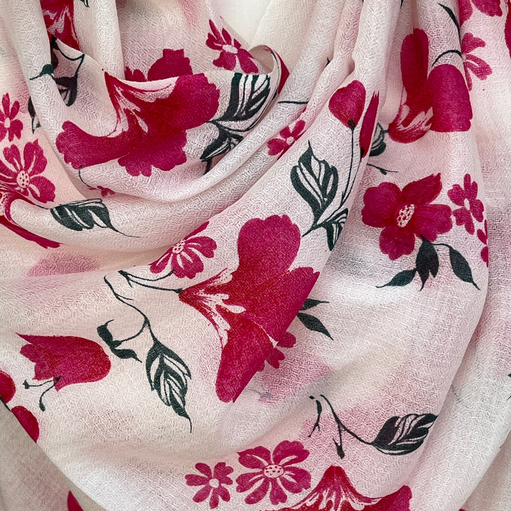 Floral cashmere scarf with pink flowers on a white background draped over a wooden mannequin against a stone wall.