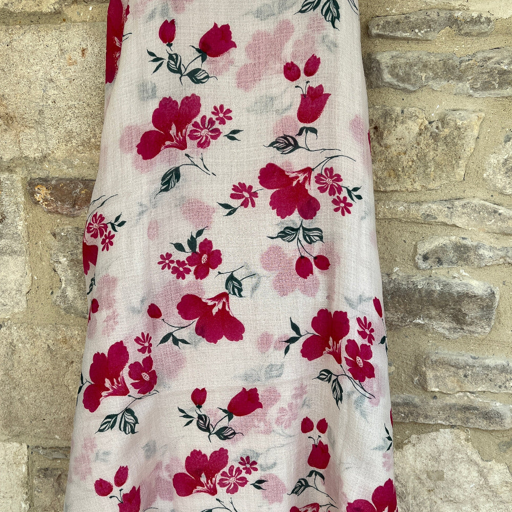 Floral cashmere scarf with pink flowers on a white background draped over a wooden mannequin against a stone wall.