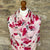 Floral cashmere scarf with pink flowers on a white background draped over a wooden mannequin against a stone wall.