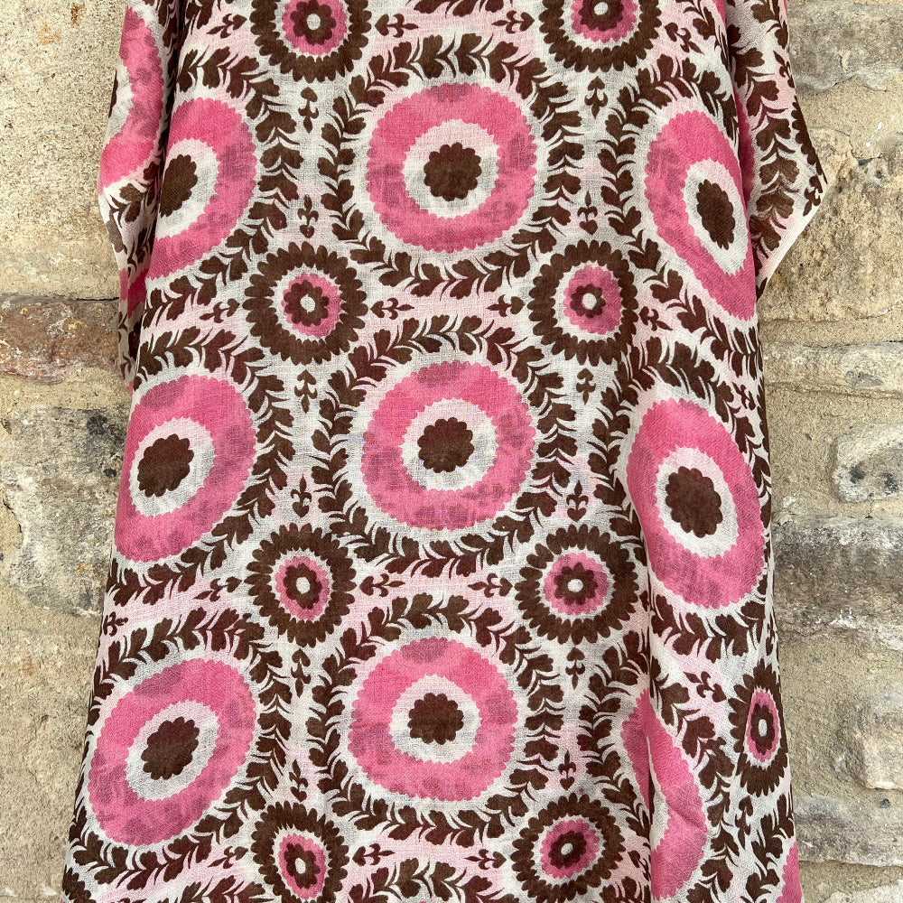 A cashmere pashmina with a pink and brown patterned against a stone wall background.