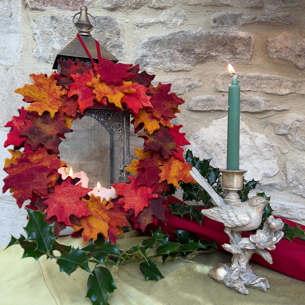 Handcrafted Felted Wool - Autumn Leaf Wreath against a stone wall with candlestick and holly decorations.