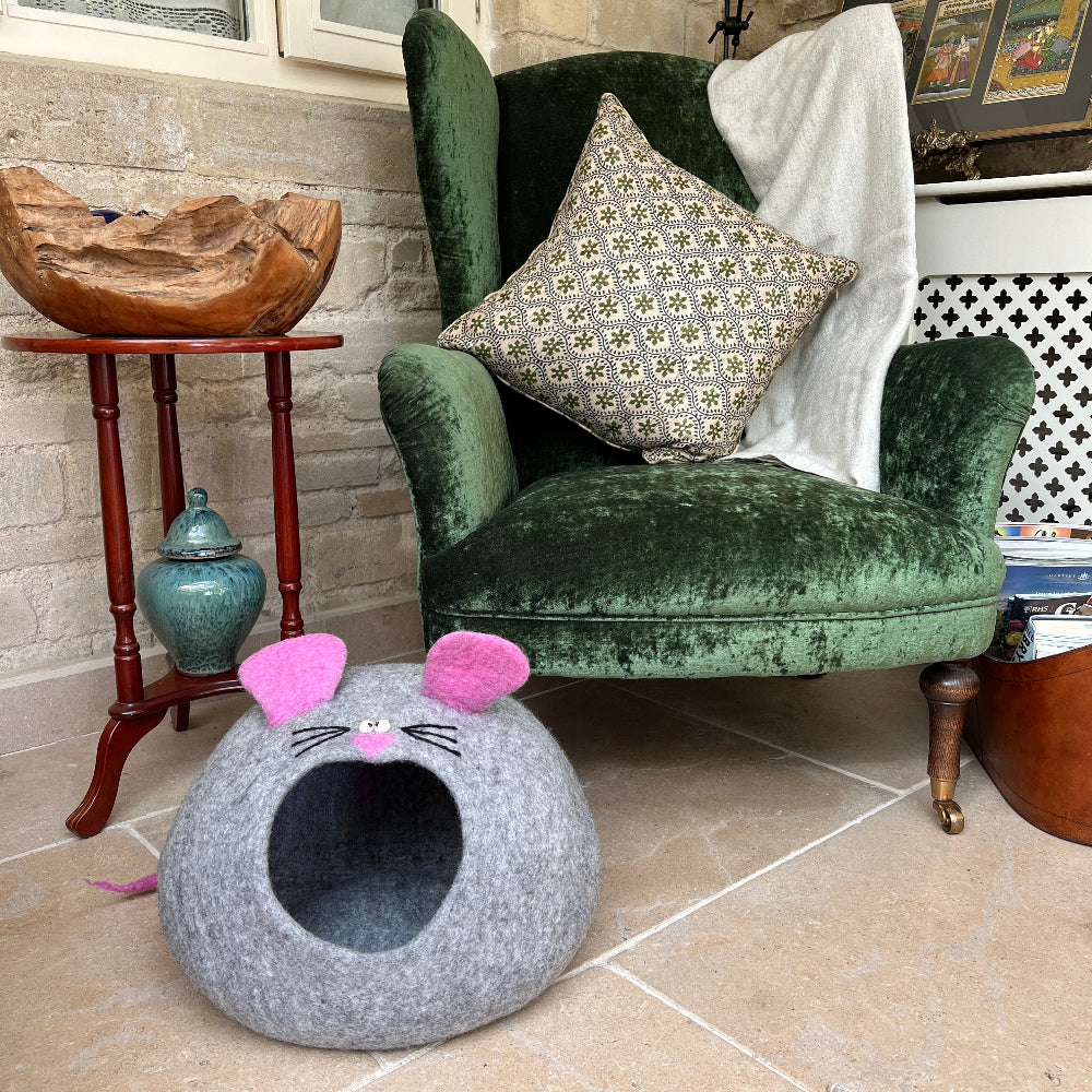 Gray 'Mouse' cat bed with pink ears and black whiskers in front of a green velvet armchair.