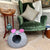 Gray 'Mouse' cat bed with pink ears and black whiskers in front of a green velvet armchair.