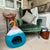 Green velvet armchair with a patterned pillow next to a blue and pink pet bed in a room with a stone wall.