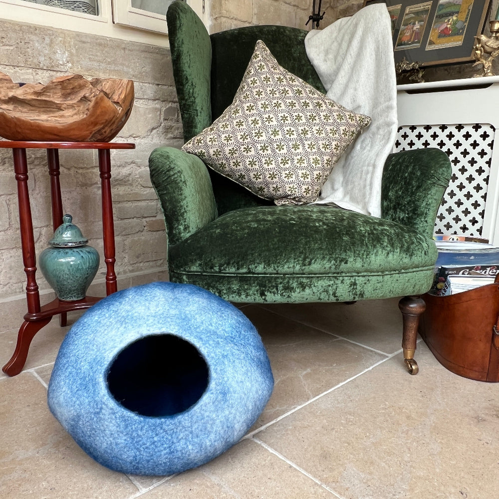 Green velvet armchair with a patterned pillow and a blue pet bed on a tiled floor.