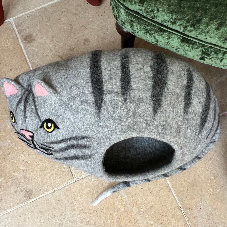 Green velvet armchair with a cat pet home in a room with a stone wall and wooden side table.