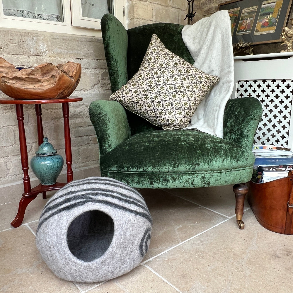 Give your pet the luxury they deserve with this handcrafted felted wool cave. Made from 100% New Zealand wool and naturally dyed, it delivers unmatched softness and breathability that keeps your companion cosy year-round. This sanctuary maintains superior air circulation for optimal comfort. At approx. 45cm wide and 30cm tall, it&#39;s the perfect size for nesting, yet folds away effortlessly when you need extra space. Beyond being a cherished pet retreat. Shown on a stone floor against a green velvet chair.
