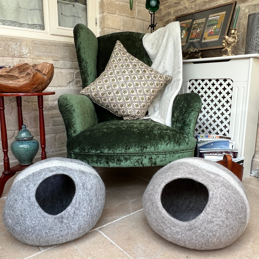 Gray pet bed  with a white stripe in front of a green velvet armchair with decorative pillows. Our handcrafted felted wool pet cave combines traditional felting techniques with premium New Zealand wool to create a versatile sanctuary for your pet.

The natural grey striped design integrates seamlessly into contemporary interiors whilst providing exceptional insulation and breathability that synthetic alternatives cannot match. Constructed entirely from pure wool and coloured with natural dyes.