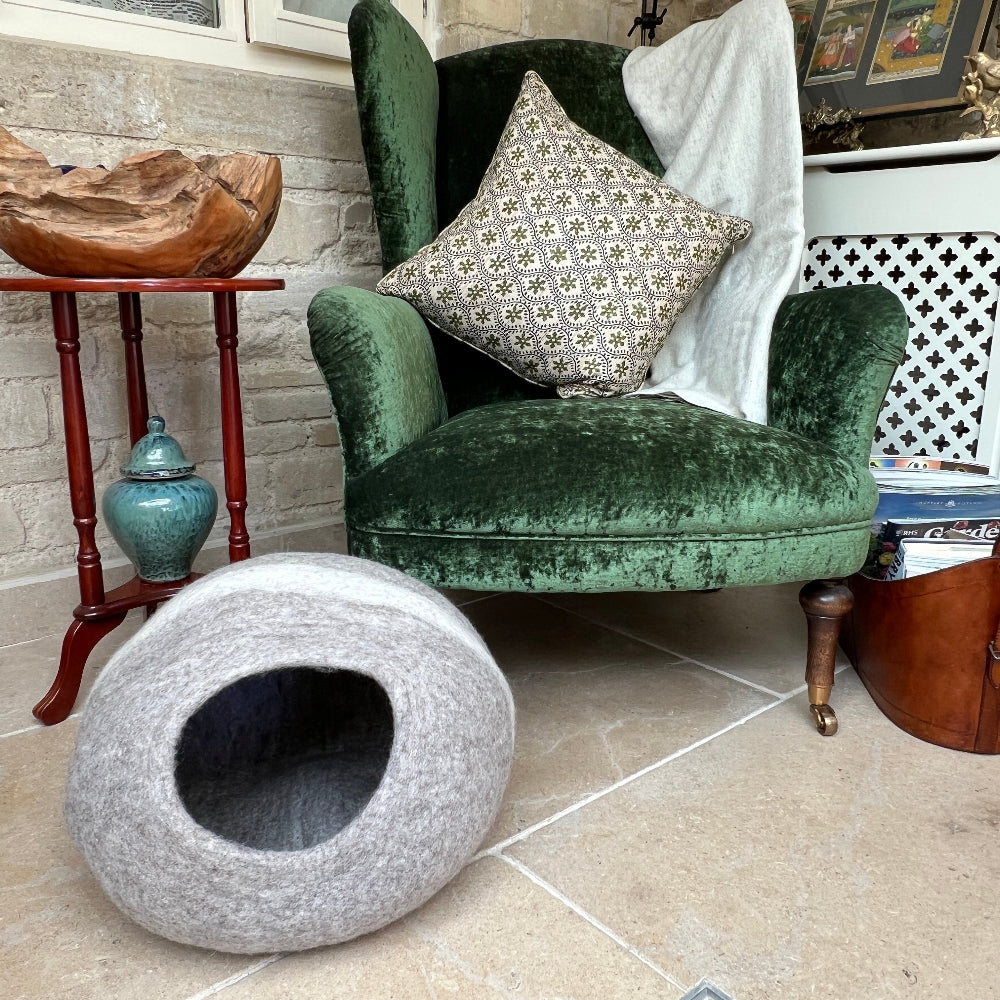 Green velvet armchair with a patterned cushion and a light brown andn cream striped pet bed on a tiled floor.