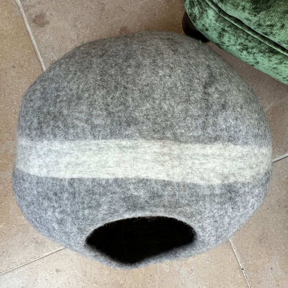 Gray pet bed  with a white stripe in front of a green velvet armchair with decorative pillows. Our handcrafted felted wool pet cave combines traditional felting techniques with premium New Zealand wool to create a versatile sanctuary for your pet.

The natural grey striped design integrates seamlessly into contemporary interiors whilst providing exceptional insulation and breathability that synthetic alternatives cannot match. Constructed entirely from pure wool and coloured with natural dyes.
