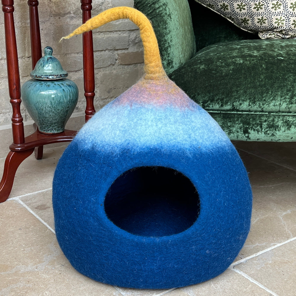Green velvet armchair with a patterned pillow and a blue multicoloured pet bed on a tiled floor.