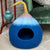 Green velvet armchair with a patterned pillow and a blue multicoloured pet bed on a tiled floor.