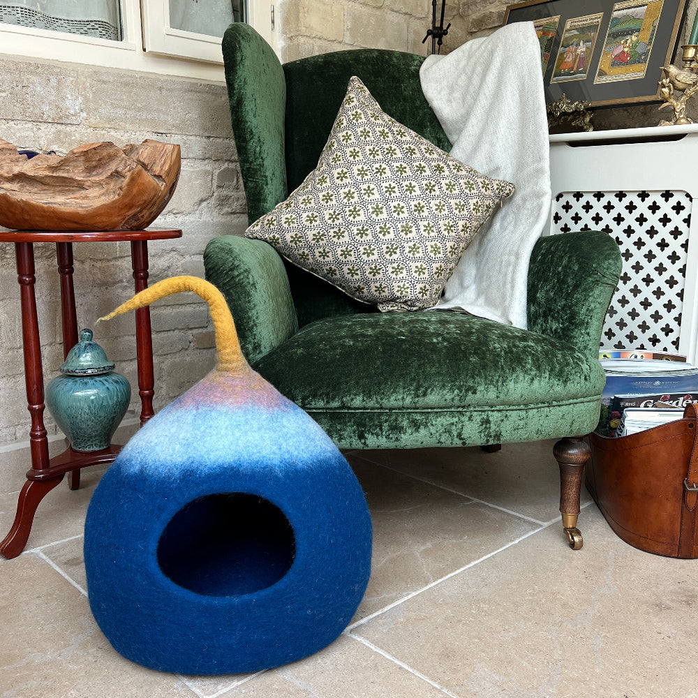 Green velvet armchair with a patterned pillow and a blue multicoloured pet bed on a tiled floor.