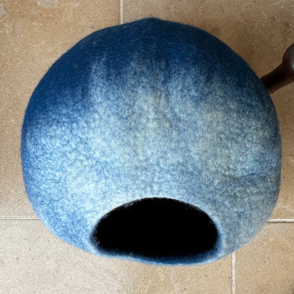 Green velvet armchair with a patterned pillow and a blue pet bed on a tiled floor.