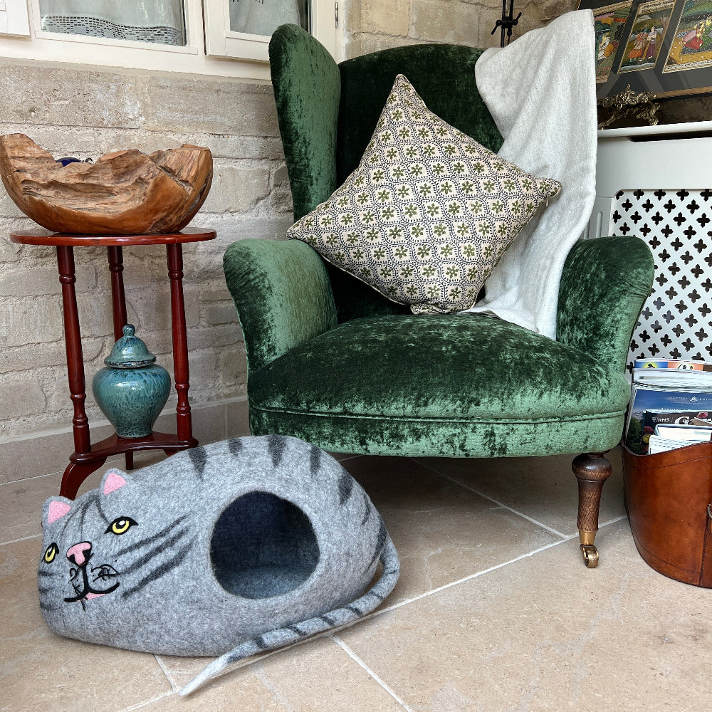 Green velvet armchair with a cat pet home in a room with a stone wall and wooden side table.