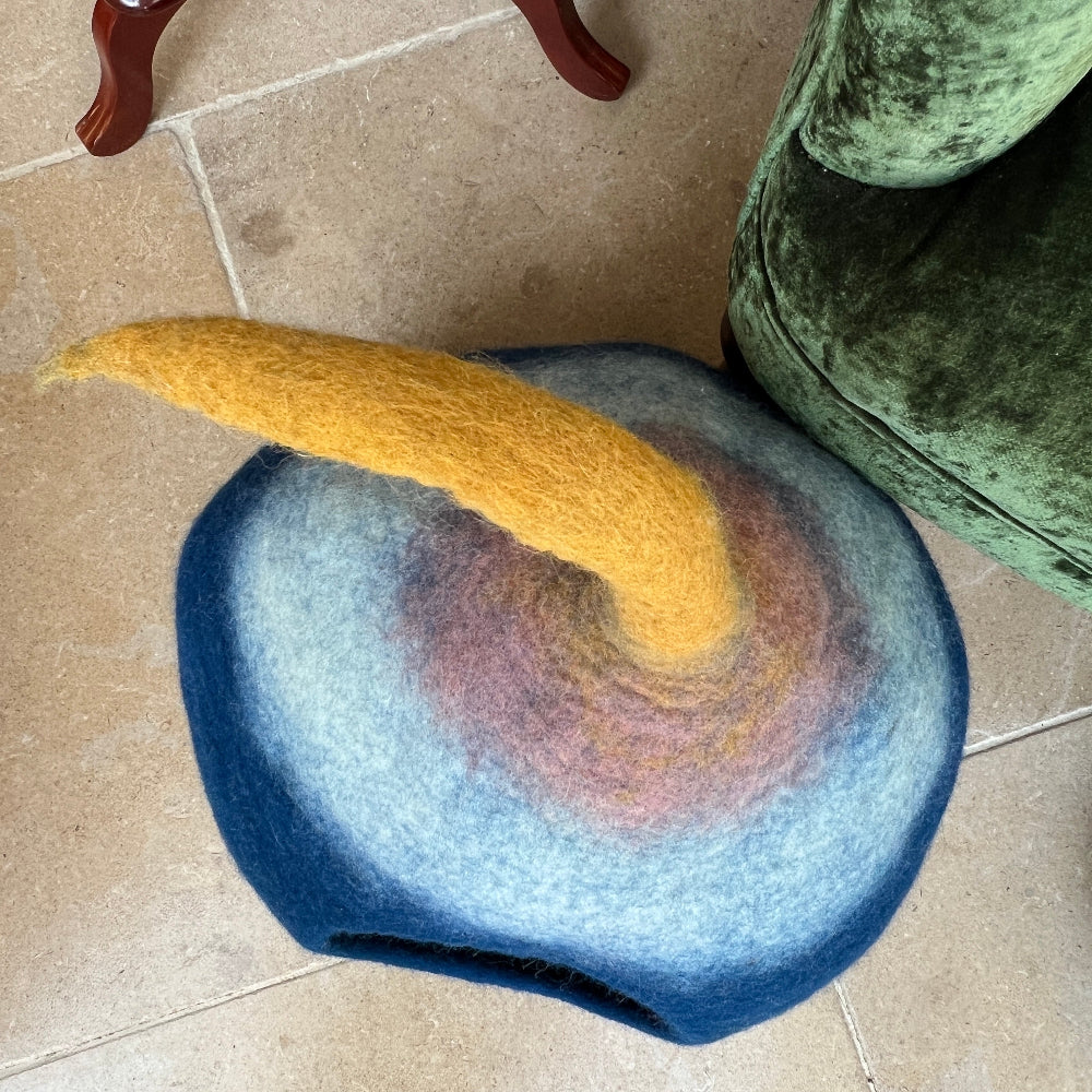 A cosy retreat for your cherished pet.

Handcrafted felted wool pet cave uses pure New Zealand wool, coloured with natural dyes. 
Inherent breathability of wool ensures optimal comfort and air circulation, whilst its natural softness and durability provide a sanctuary your pet will treasure. Beyond its primary function as a pet bed, this versatile piece serves as elegant storage or decorative accent. Shown on a stone floor against a green armchair with a  cashmere blanket and magazines. 