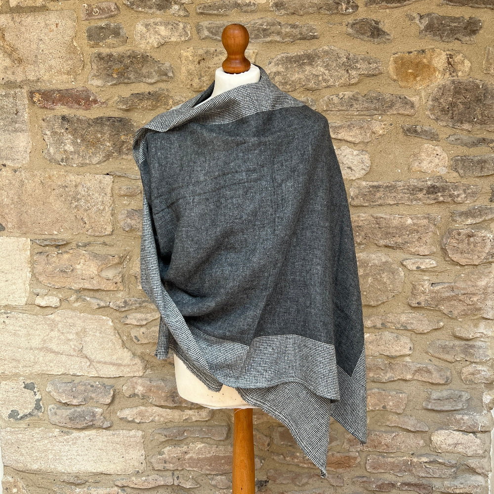 Handwoven Cashmere &amp; Wool Reversible Pashmina - Grey &amp; Black.  Gray reversible patterned cashmere scarf draped over a mannequin against a stone wall background