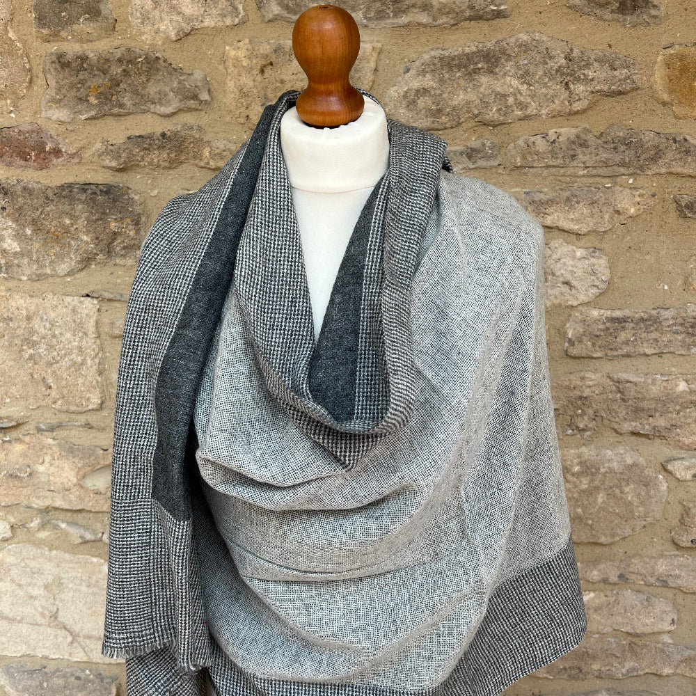 Handwoven Cashmere & Wool Reversible Pashmina - Grey & Black.  Gray reversible patterned cashmere scarf draped over a mannequin against a stone wall background