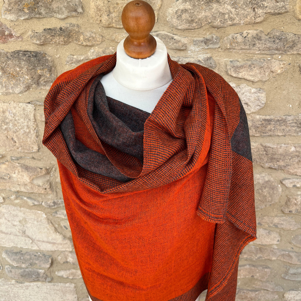 Handwoven Cashmere &amp; Wool Reversible Pashmina - Orange &amp; Grey shown on a mannequin against a cotswold stone wall background